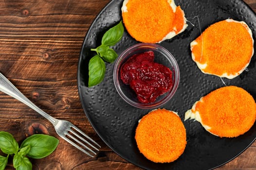 Homemade baked or fried camembert cheese with berry sauce on rustic wooden surface.