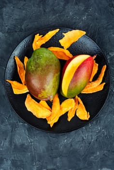 Dried mango pieces with knife and raw fruits. Top view.