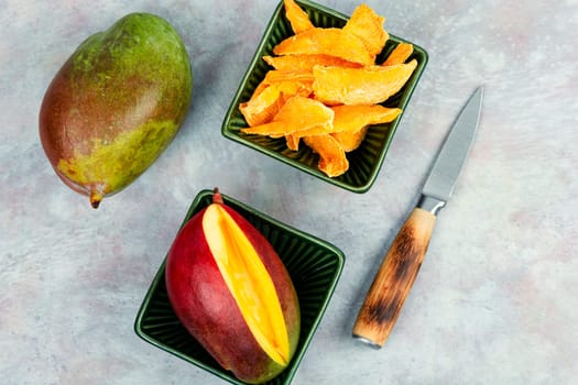 Dried mango pieces with knife and raw fruits. Top view.