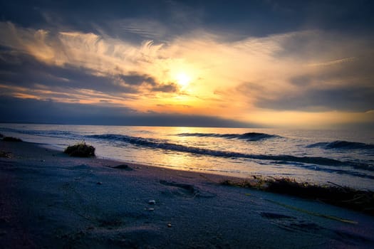 Sunset, illuminated sea. Sandy beach in the foreground. Light waves. Baltic Sea. Landscape on the coast