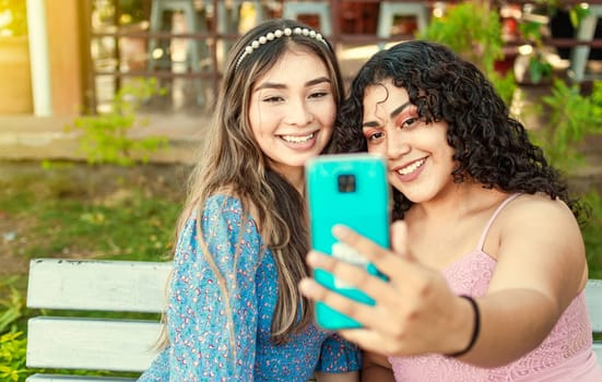 Close up of two smiling teenage girlfriends sitting on a bench taking a selfie, Two smiling teenage girlfriends taking a selfie sitting on a bench at sunset