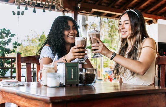 Two teenagers girls having a milkshake, two smiling girls friends in a cafe, two girls toasting in a cafe