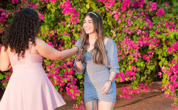 Two girls friends waving and shaking hands, two smiling girls shaking hands on the street