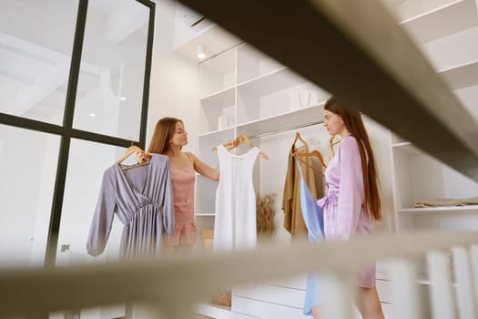 Cute girl friends choosing casual attire for party at home. Charming millennial woman preparing for dating. Concept of friendship and support