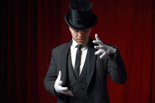 Waist-up portrait of handsome man magician showing mysterious trick waving his hands in white gloves on stage scene. Magical show performance and enchantment of audience