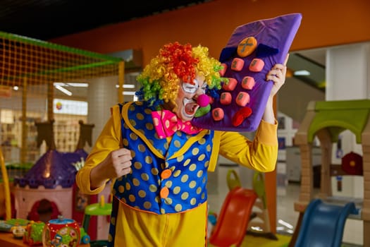 Funny crazy clown talking loudly huge toy mobile phone while entertaining at playroom. Portrait of carefree comedy actor playing games gesturing emotionally and screaming