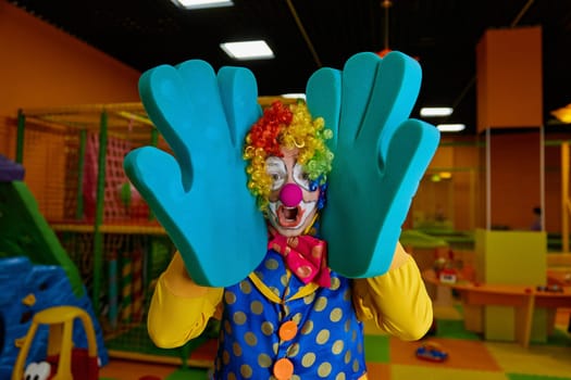 Funny clown with foam hands posing for camera showing happiness and little craziness. Emotional artist wearing colorful wig and costume performing comedian program for kids
