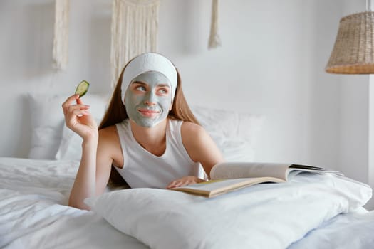 Portrait of young smiling woman enjoying home spa procedure. Millennial female applying clay mask and cucumber eye patches for skin care. Beauty treatment concept