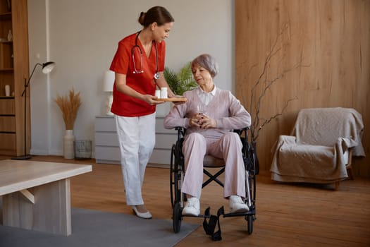 Senior lady receiving pills from woman healthcare worker at nursing home. Old female patient undergoing rehabilitation at medical hospice