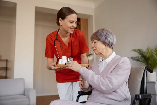 Senior lady receiving pills from woman healthcare worker at nursing home. Old female patient undergoing rehabilitation at medical hospice