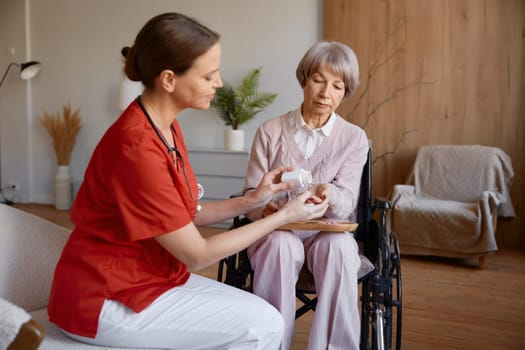 Woman nurse caregiver giving pills to old woman for healthcare support. Medical help and retirement health insurance for elderly people at nursing home concept