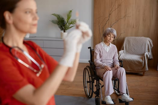 Qualified professional woman nurse preparing syringe for vaccination of old lady patient at retirement house. Medicinal injection for elderly people during corona or flu outbreak