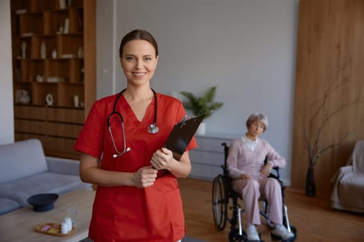 Portrait of friendly smiling woman doctor or nurse at nursing home. Professional medical worker or caregiver holding patient card providing healthcare support at hospice for elderly people