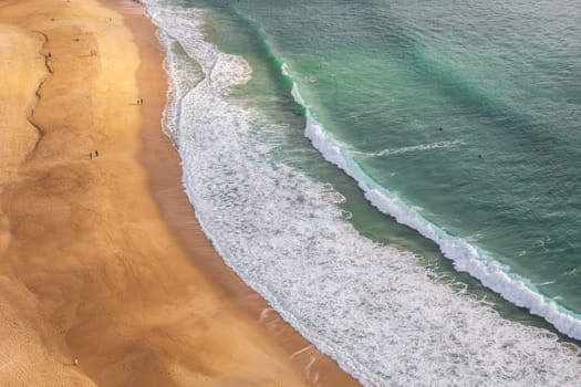 Aerial view of the sandy beach and the turquoise waves of the Atlantic ocean in Nazaré, Portugal