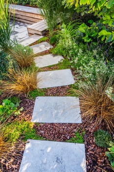 Garden path with stone slabs with bark mulch and native plants. Landscaping and gardening concept.