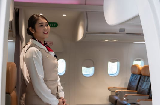 Cheerful air hostess or cabin crew standing at airplane entrance door. Flight attendant waiting for passengers to board. Airline transportation and tourism concept.