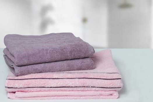 Table top on towels background. Closeup of a stack or pile of violet and pink soft terry bath towels at a bright table against blurred bathroom background. Space.