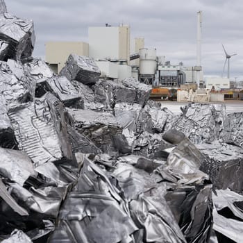 Pressed scrap metal at a scrap yard in the port of Magdeburg in Germany, a factory in the background