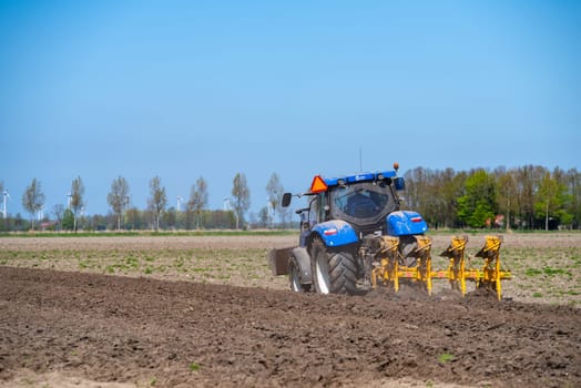 EMMELOORD, NETHERLANDS - APRIL 21, 2018: Farmer with his tractor plowing his land in early spring