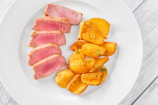 Portion of tuna with potato dippers on the plate