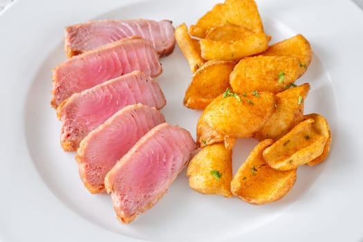 Portion of tuna with potato dippers on the plate