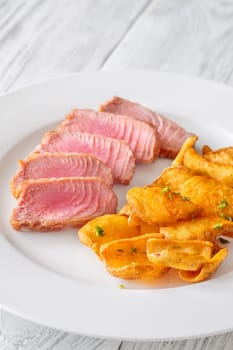 Portion of tuna with potato dippers on the plate