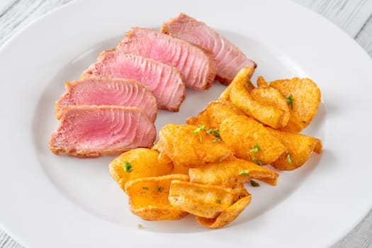 Portion of tuna with potato dippers on the plate
