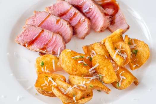 Portion of tuna with potato dippers on the plate