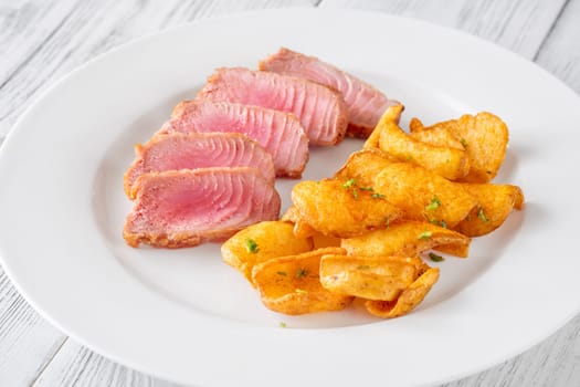 Portion of tuna with potato dippers on the plate