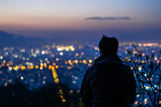 A man is standing on top of a hill, overlooking a sprawling city below. He gazes at the urban landscape, with buildings, roads, and skyscrapers visible in the distance.