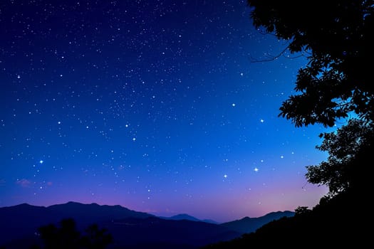 The night sky above mountain peaks is illuminated by countless stars, creating a breathtaking celestial display. The mountains stand tall and dark against the twinkling sky, emphasizing the vastness and beauty of the natural world.