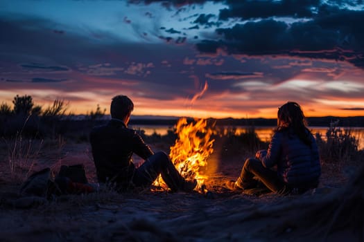 A man and a woman are sitting next to a crackling fire, surrounded by darkness. They appear relaxed and engaged in conversation, with the warmth of the flames illuminating their faces.