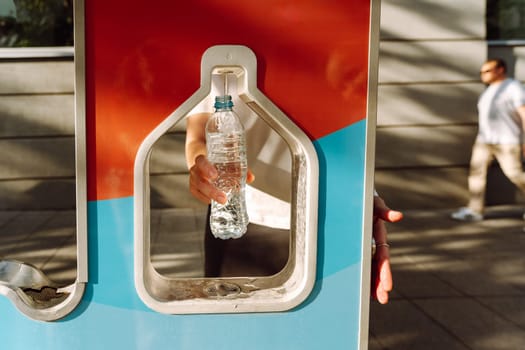 Man refilling his water bottle at the city. Free public water bottle refill station. Sustainable and green city. Male in black coat. Tap water to reduce plastic bottle usage. Drinking water dispenser
