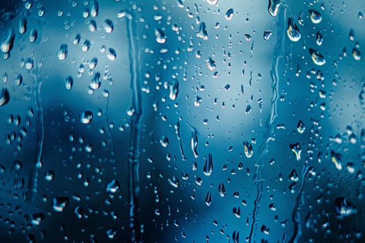 Rain drops are visible on a window, with a clear blue sky in the background. The drops are forming irregular patterns as they trickle down the glass surface, reflecting the light from the sky.