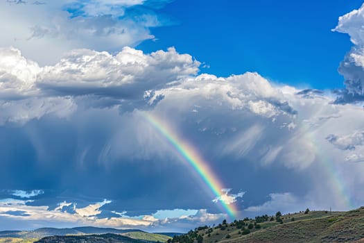 A rainbow arching across a cloudy sky above a picturesque valley. The vibrant colors of the rainbow stand out against the backdrop of the grey clouds, creating a striking contrast in the scenery.