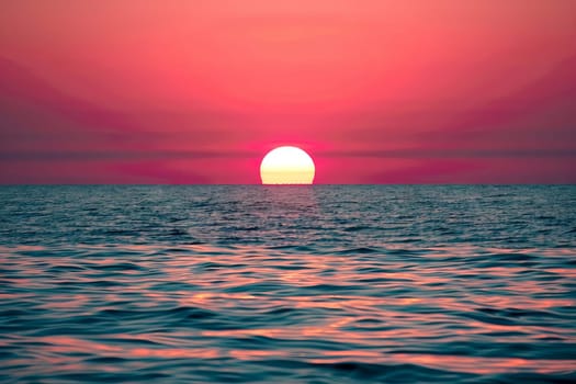The sun is descending below the horizon, casting a warm golden glow over the vast ocean. Waves gently roll towards the shore as the sky transitions from blue to orange and pink hues.