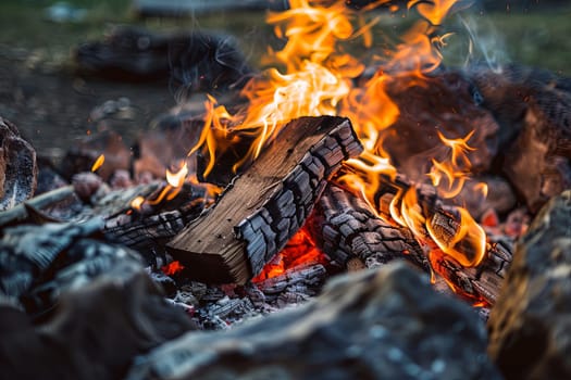 A close-up view of a roaring fire, surrounded by rocks and grass in the background. The flames flicker and dance, casting a warm glow on the rocky terrain and green vegetation.