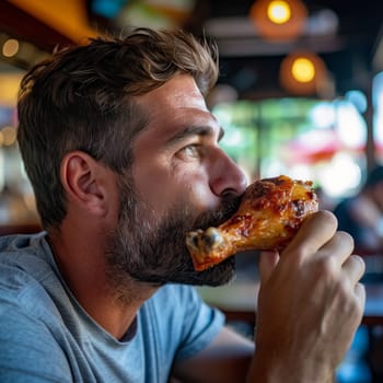 A man with a beard enjoys a succulent chicken drumstick, savoring the moment in a casual dining setting