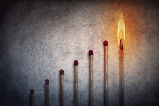 Match sticks arranged in shape of a increasing graph with the top one matchstick burning in flame. Financial chart metaphor background showing business growth or leadership concept