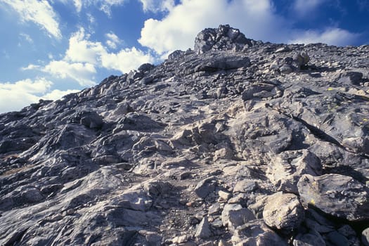 A rocky mountain dominating the scene with various sizes of rocks scattered around it. The sky serves as a backdrop, adding contrast to the rugged terrain.