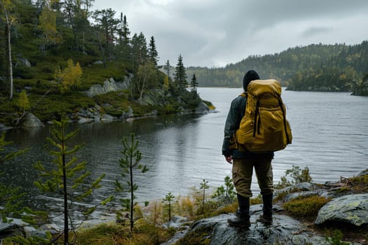 A man wearing a backpack stands on a rocky shore. The rugged terrain contrasts with the calm sea in the background. The man appears to be contemplating the vastness of the ocean.