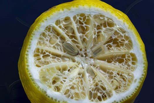 A lemon has been cut in half, revealing its juicy interior, placed on a black surface. The vibrant yellow color of the lemon contrasts sharply with the dark background.