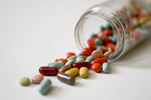 Multiple pills of various colors spilling out of a glass jar onto a wooden table. The pills are scattered around in disarray, creating a sense of chaos.