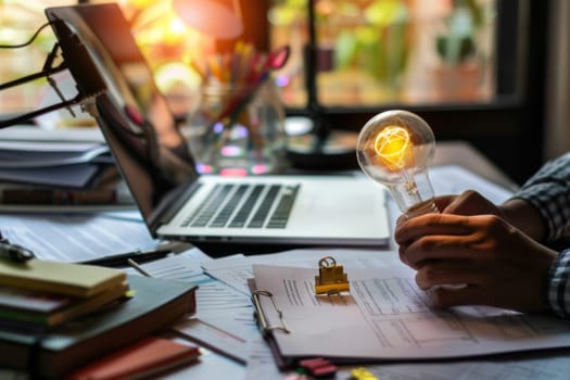A person is holding up a light bulb over a laptop computer, as if having an idea or working on a creative project. The laptop screen is illuminated by the light from the bulb.