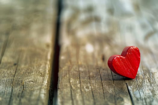 A red heart-shaped object is placed on top of a wooden table, showing a contrast between the vibrant color and natural wood texture.