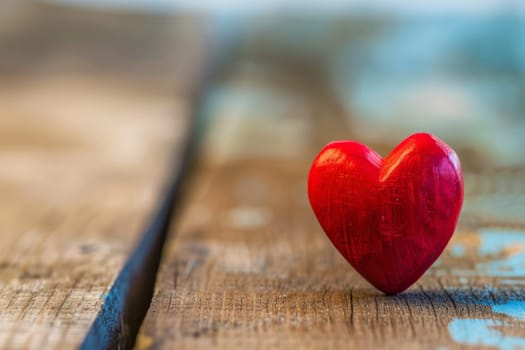 A red heart-shaped object resting on a wooden table, creating a simple yet striking visual contrast. The heart stands out against the rustic background, emphasizing its vibrant color and symbolic significance.