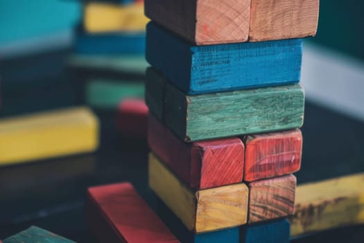 A pile of wooden blocks is neatly arranged on top of a wooden table. The blocks vary in size and shape, creating a structured yet dynamic composition in the frame.