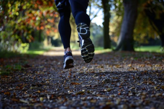 A person is seen running energetically on a dirt trail surrounded by dense trees in a forest setting. The runner is focused and determined, with sunlight filtering through the foliage above.