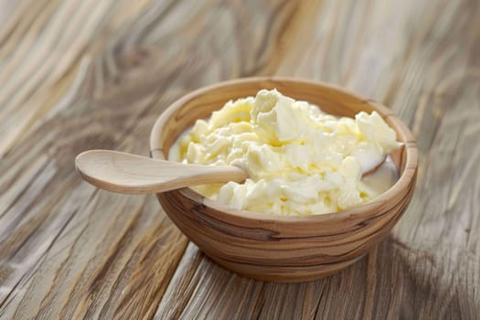 A wooden bowl filled with fluffy whipped cream sits atop a rustic wooden table. The whipped cream is perfectly swirled and looks inviting and delicious.