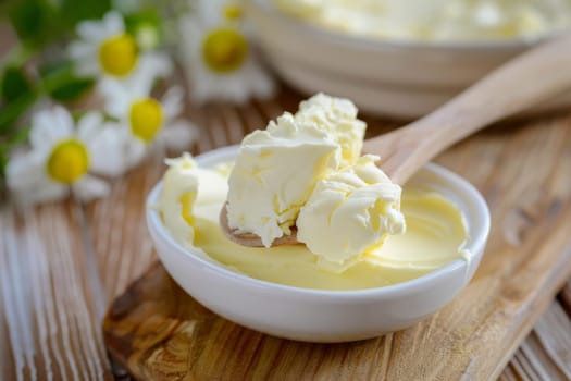 A bowl filled with cream is placed on top of a wooden table. The cream is smooth and looks inviting, contrasting with the rustic texture of the table.